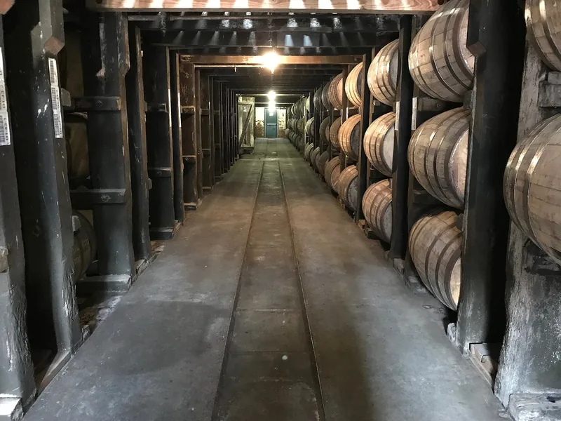 Inside a barrel-ageing warehouse, barrels racked either side of the aisle